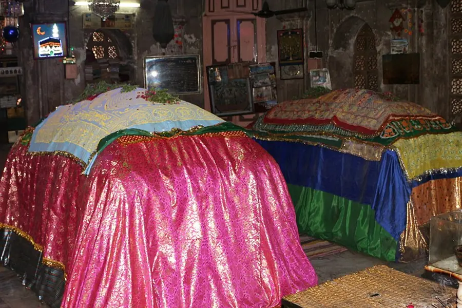 Tombs draped in bright pink, green and gold cloth inside a low chamber