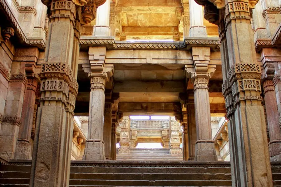 Carved stone pillars descending in tiers into a stepwell, lit from the opening above
