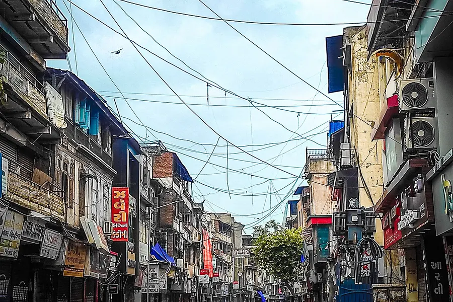 A narrow market street crowded with shopfronts, signs and overhead wiring