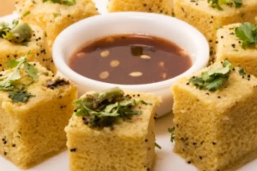 Cubes of dhokla with coriander beside a bowl of dark chutney