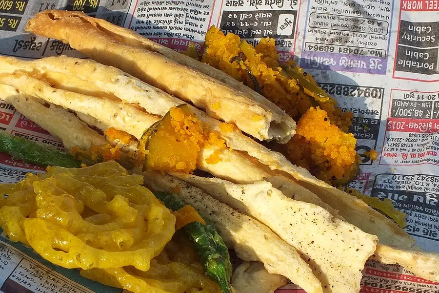 A plate of crisp fafda strips with jalebi and chutney at a street stall
