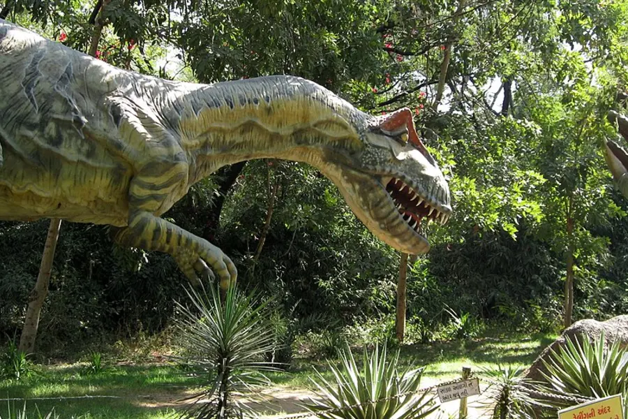 A life-size model dinosaur standing among trees in a park