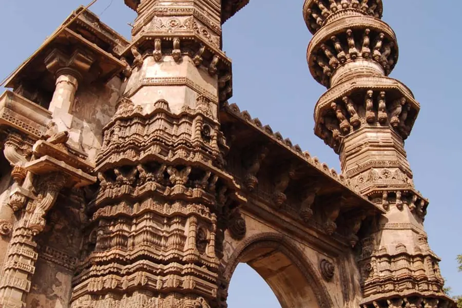 Two heavily carved sandstone minarets rising above an arched gateway