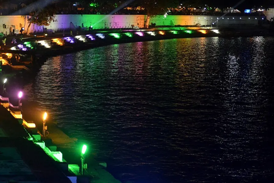 A lakefront at night, a bridge and railings lit in green and purple