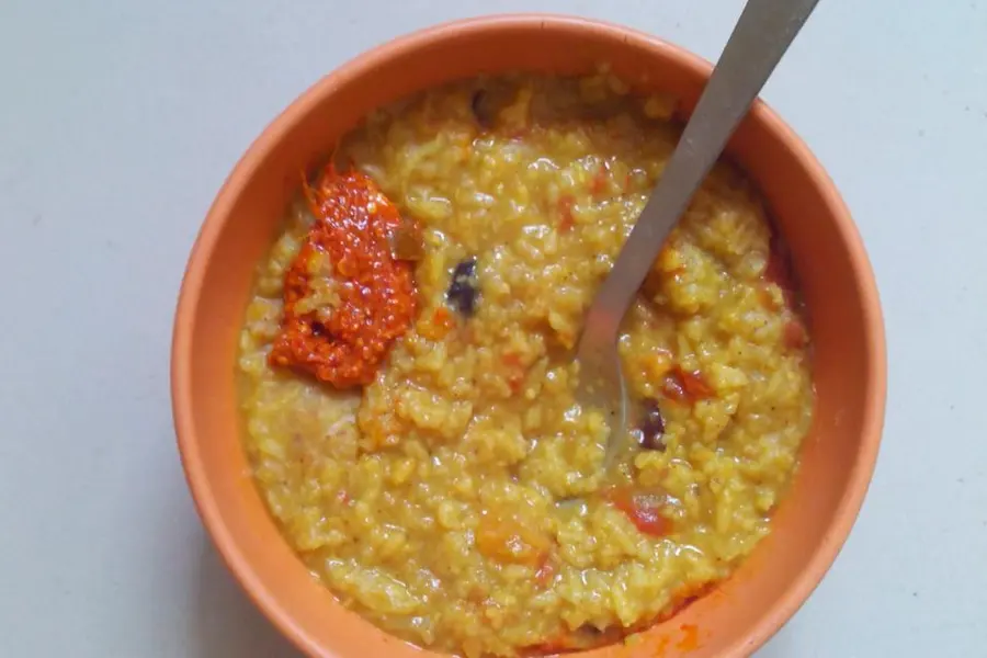 A bowl of khichdi topped with pickle, a spoon standing in it