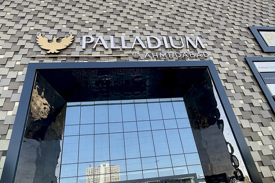 The glass and stone entrance of the Palladium mall with its lit sign