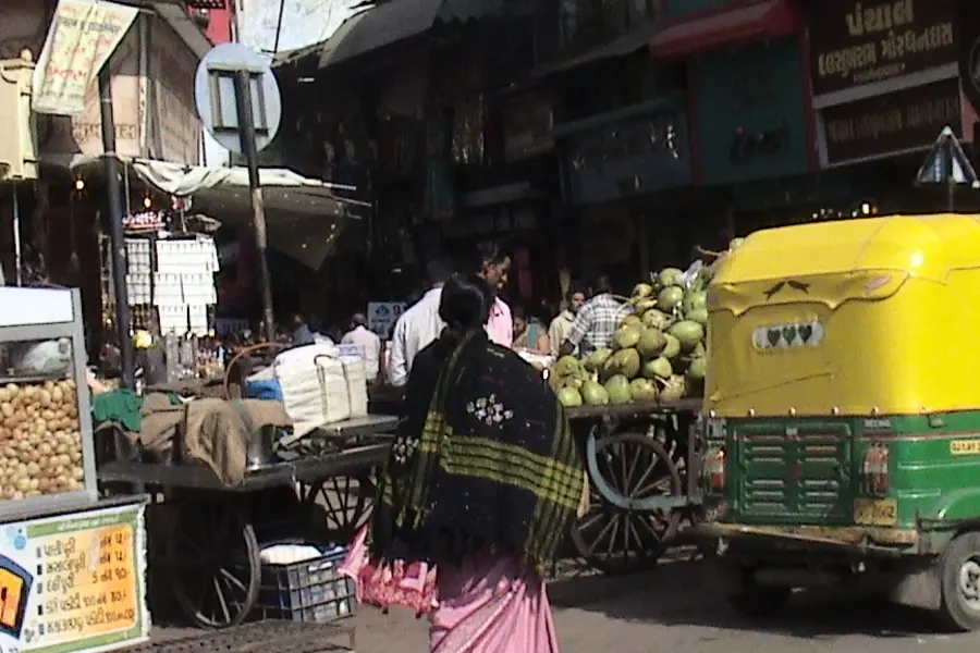 A market lane with a fruit cart, an auto rickshaw and shoppers