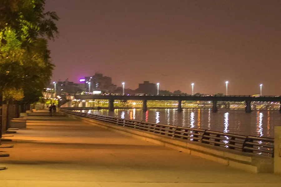 The riverfront promenade at night, lamps reflecting off the water