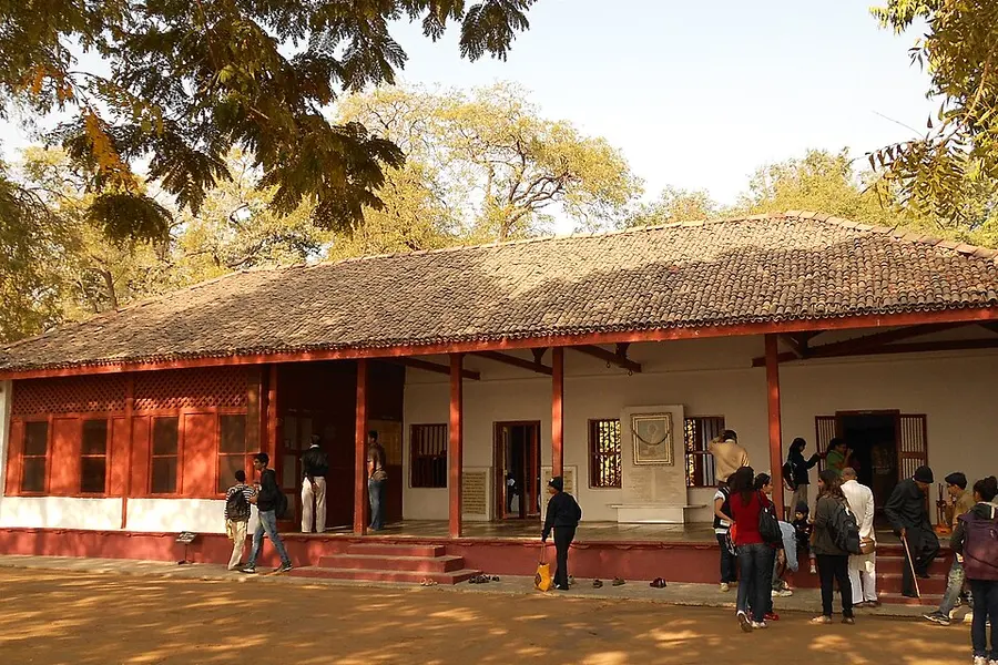 The low tiled-roof verandah of the ashram with visitors walking under the trees