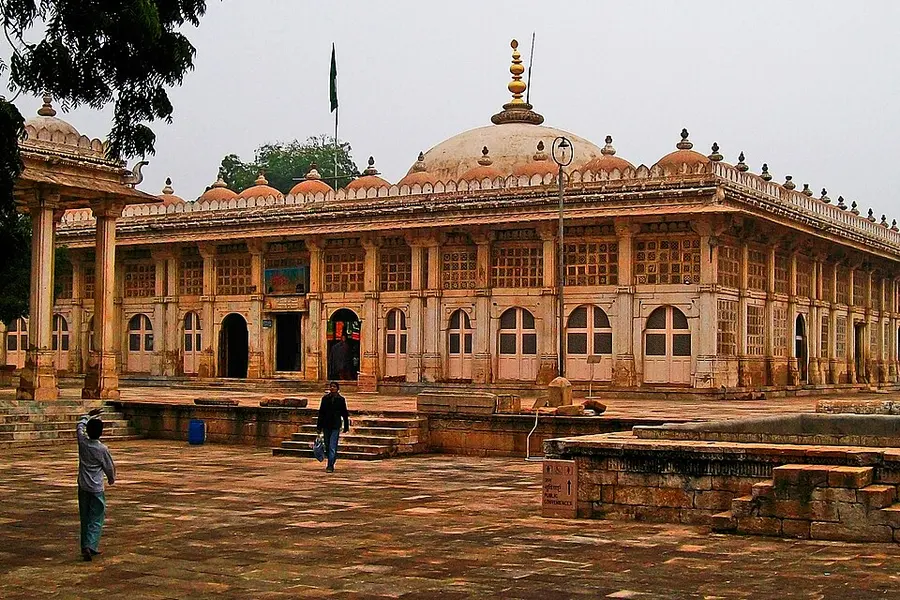 A domed stone pavilion and arcaded hall at Sarkhej Roza across an empty paved court