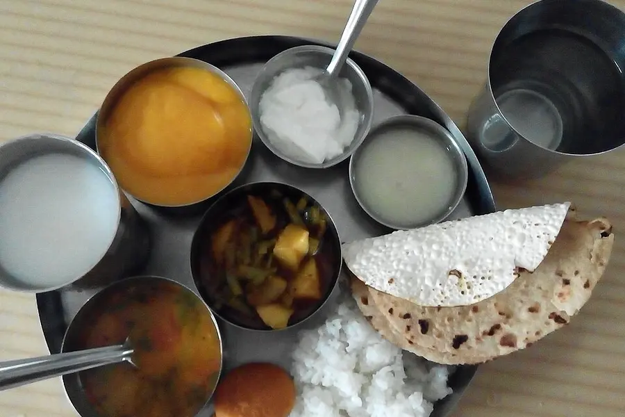 A steel thali of small bowls with buttermilk, papad and rotli