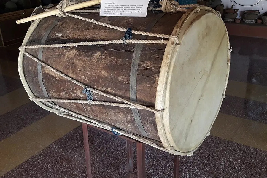 A long double-headed dhol drum on a stand in a museum display case
